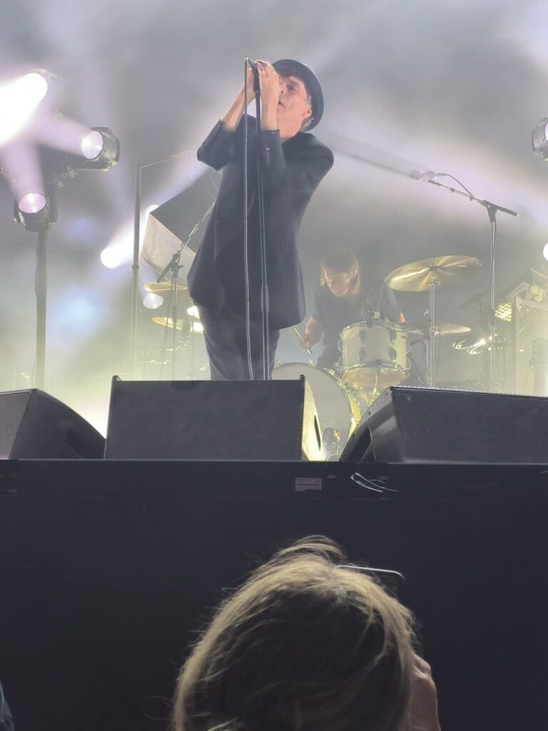 Thåström singing into a microphone on a smoke-infused stage in Karlstad, illuminated by dramatic lights
