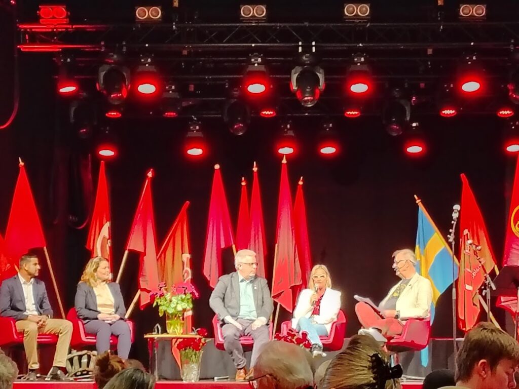 Monday presence everyday life from the weekend – Social Democrats campaign kickoff with a panel on stage, red flags and the Swedish flag in the background.