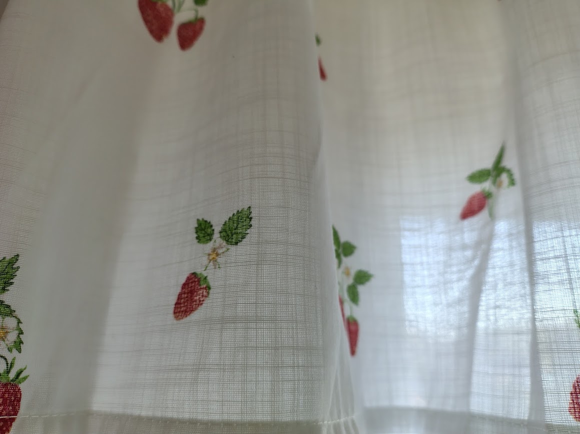 Close-up of white curtains with small red strawberries and green leaves – a personal blog post about home, change and peaceful everyday living